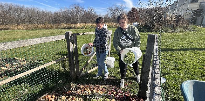 Sarah Joy '26 and Patrick Cross '24 toss pre-consumer food waste into the composting bin at Susquehanna's Campus Garden.